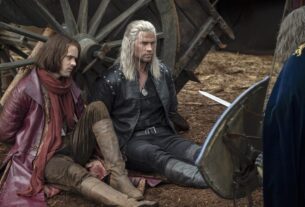 Geralt sits near a wagon of hay.