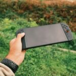 Mão segurando console portátil ao ar livre, como o Nintendo Switch 2
