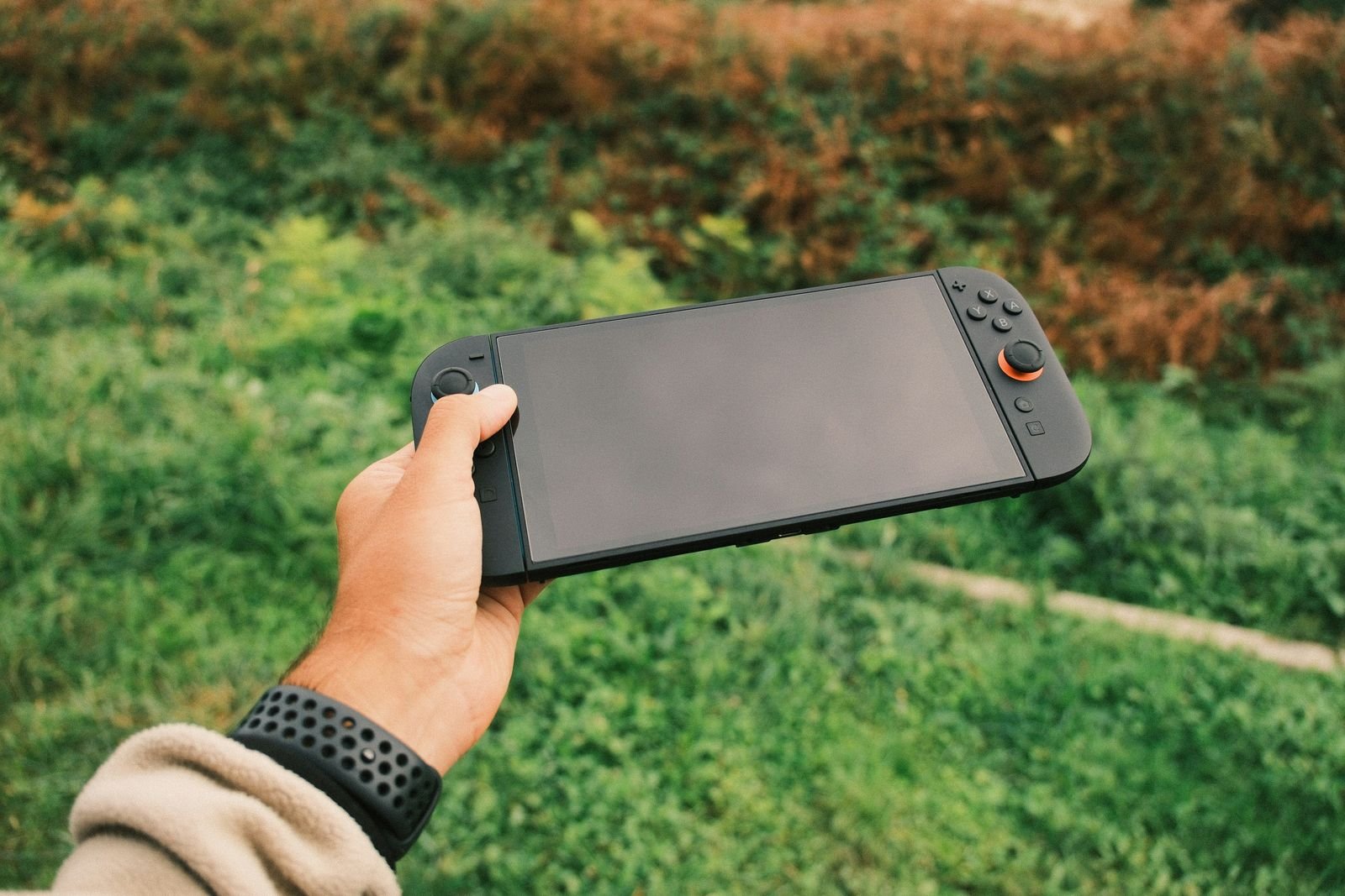 Mão segurando console portátil ao ar livre, como o Nintendo Switch 2